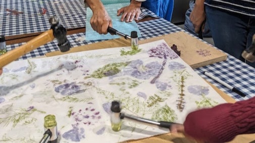 A close up of hands hammering flowers onto fabric to create an imprint.